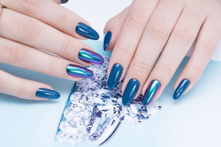 Mains avec vernis bleu irisé illustrant une manucure parfaite à la maison élégante