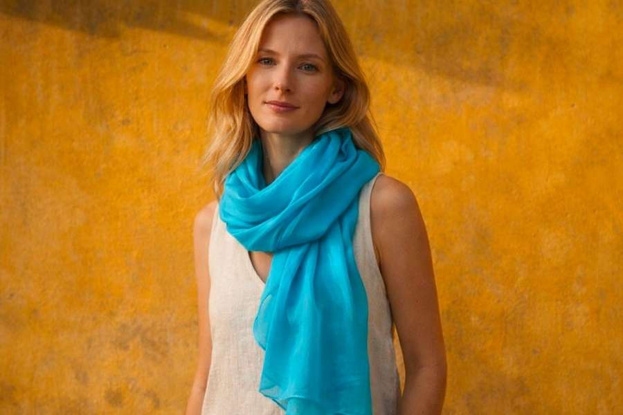 Portrait d'une femme blonde portant un long foulard rectangulaire bleu vif drapé avec fluidité sur une robe claire.