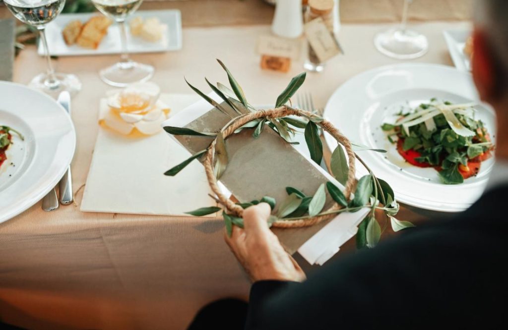 Invité tenant le menu de mariage orné d'olivier à une table dressée par un traiteur bio et local pour mariage.